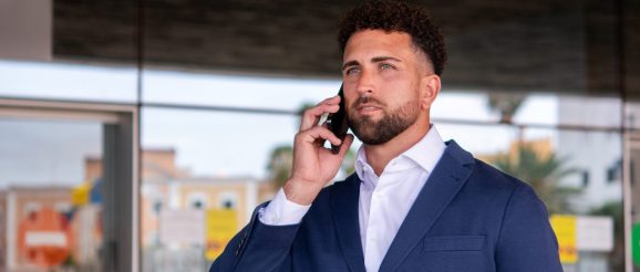 Commercial en pleine téléprospection, assis à son bureau avec un téléphone et un ordinateur.