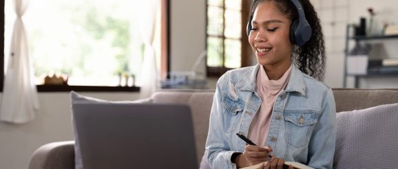 Personne suivant une formation d’assistant virtuel sur un ordinateur portable, avec un carnet de notes à côté.