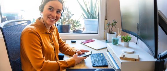 Téléprospectrice freelance travaillant au téléphone devant son ordinateur, avec un carnet de suivi commercial sur le bureau.