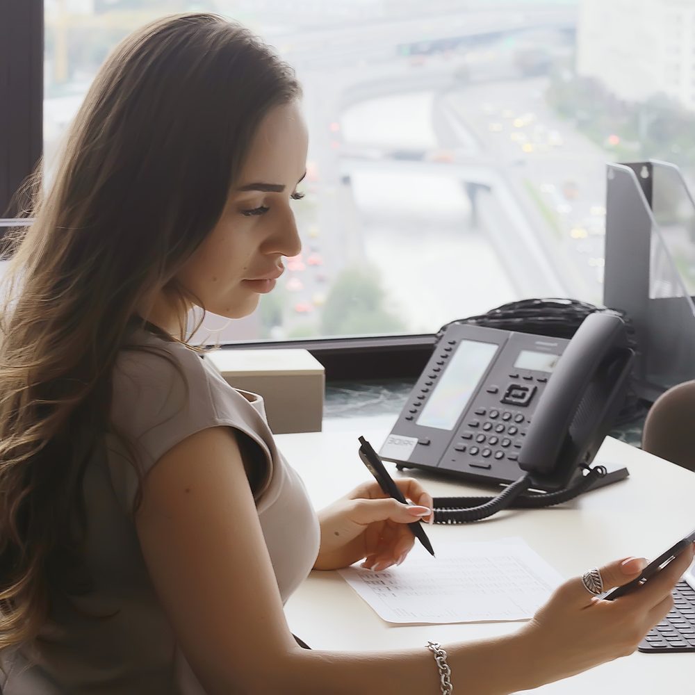 Professionnel de la téléprospection comparant une offre d’emploi et sa rémunération à son bureau.